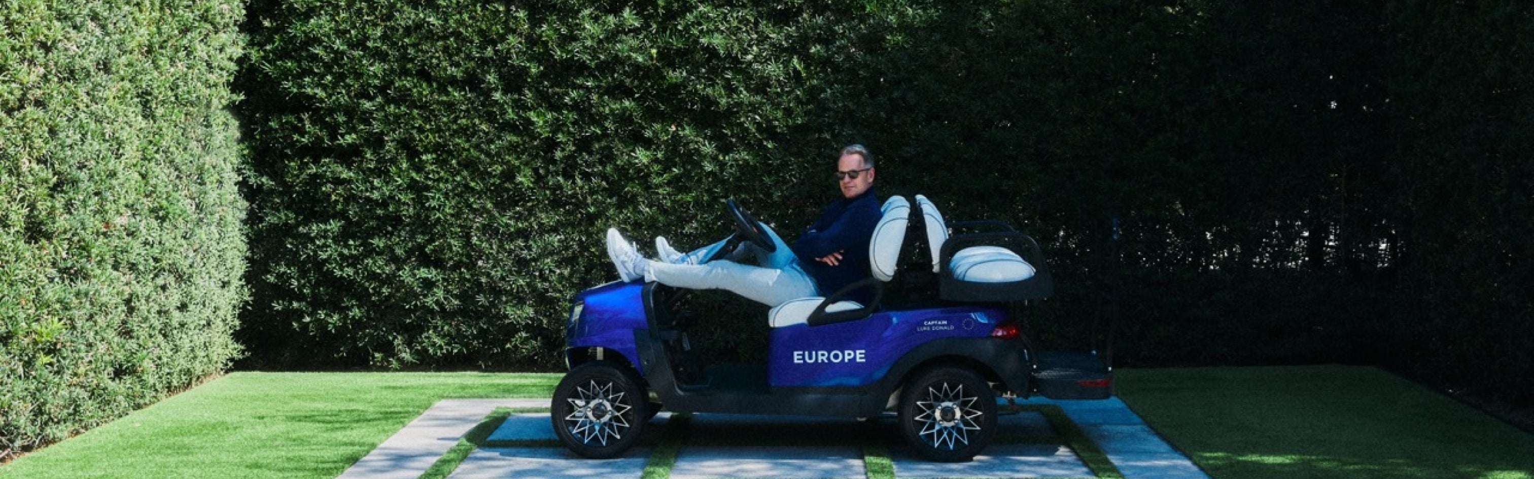 European Ryder Cup Captain Luke Donald sitting in a golf cart with 'Europe' branding on a grassy area.