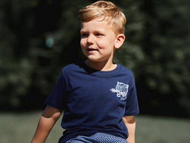 Young boy wearing a navy blue t-shirt with a logo, sitting outdoors with a blurred green background