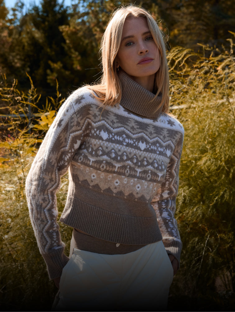 Woman wearing a patterned sweater standing in a field with trees in the background