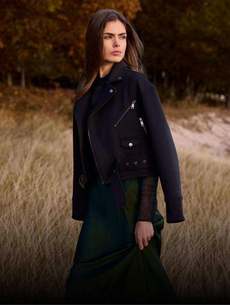 Woman wearing a dark coat standing in a field with trees in the background