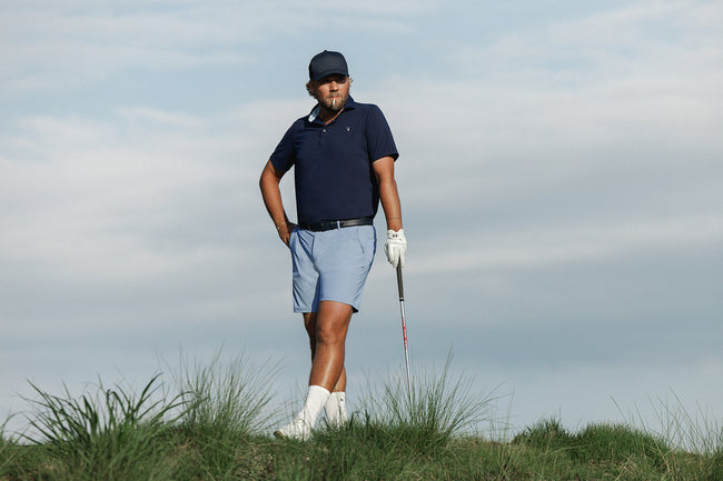 Man in golf attire standing on a grassy area with a golf club