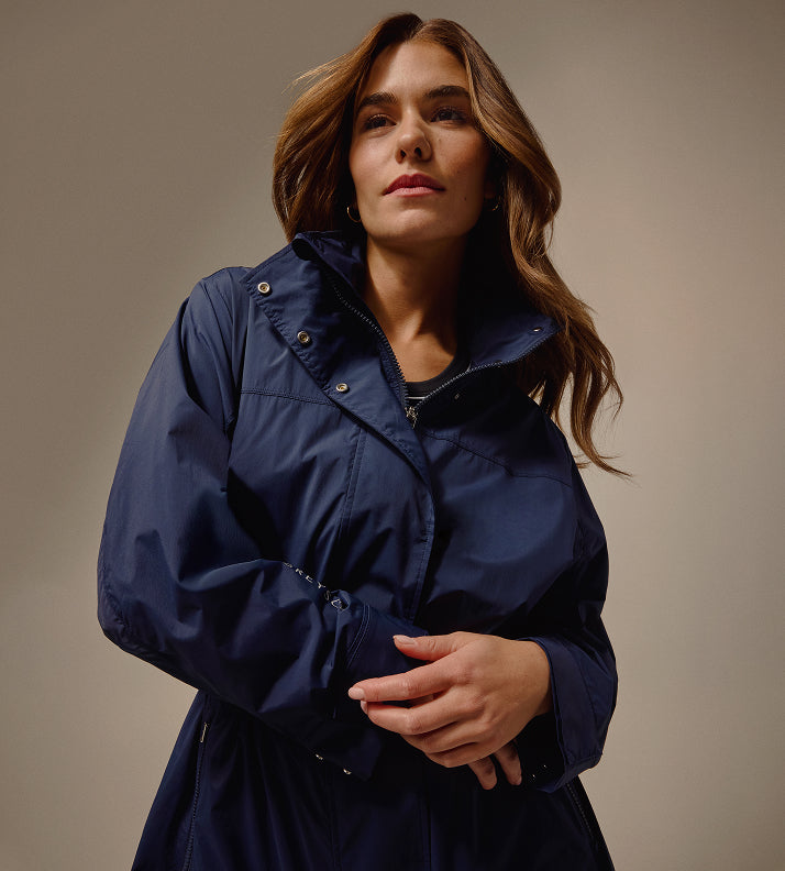 Woman wearing a navy blue raincoat against a neutral background